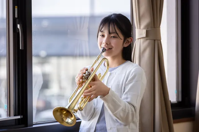 窓辺でトランペットを演奏する吹奏楽部の女子生徒